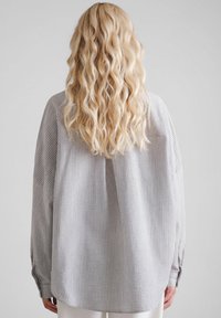 Koszula w kratę o luźnym kroju, w jasnoszarym i białym kolorze, z długimi rękawami i miękką, teksturowaną tkaniną.