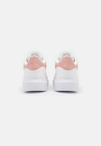 Zapatillas blancas con parte superior de cuero suave y acento de talón de gamuza rosa. Suela de goma blanca gruesa; diseño minimalista y forma redondeada.