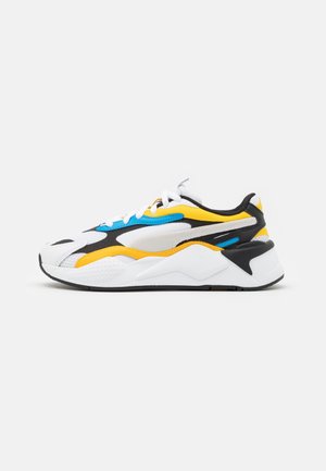 Biały sneaker z żółtymi, niebieskimi i czarnymi akcentami, grubą podeszwą i sznurowanym fasonem, pokazany z boku na jednolitym tle.