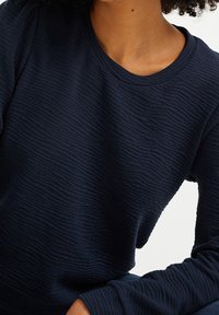 Mörkblå texturerad sweatshirt med rund hals och långa ärmar, som har ett subtilt vågmönster på tyget. Mjuk bomullsblandning.