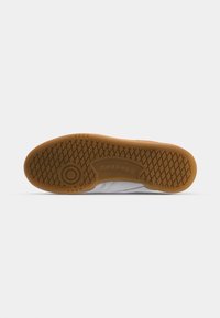 Fehér tornacipő talpa texturált gumimintával. Jellemzői a barna ragasztott gumitalp, sima élek és a Reebok logó részlet.