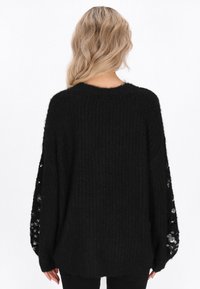 Czarny oversize sweter z teksturowanym splotem, z cekinowymi akcentami na rękawach i szerokim, luźnym krojem.