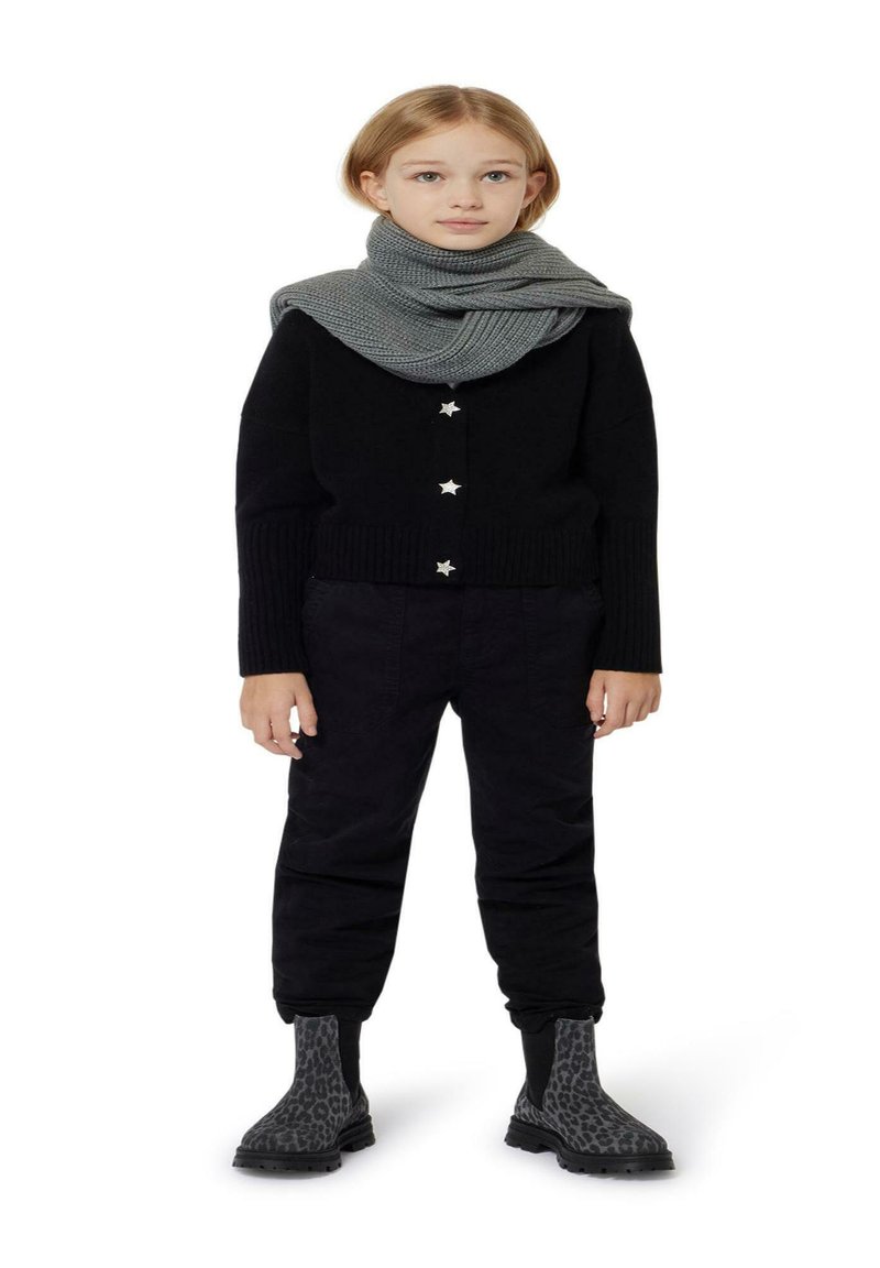 Zwarte gebreide cardigan met stervormige knopen, gecombineerd met zwarte broek en een grijze gebreide sjaal. De laarzen hebben een luipaardprint ontwerp.