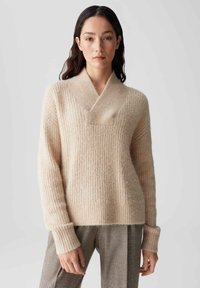 Beige gebreide trui met een sjawl kraag, geribbelde textuur en brede manchetten. Draagt over geruite broeken, biedt een relaxte pasvorm.