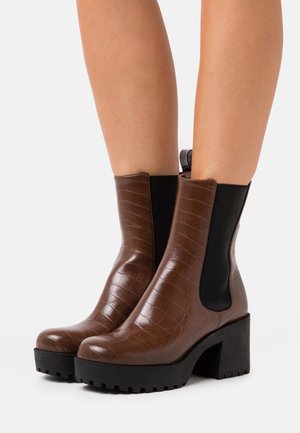 Braune, krokodilpräge Ankle Boots mit schwarzen elastischen Seitenpaneelen und einem stabilen schwarzen Absatz, mit abgerundetem Zehenbereich und strukturierter Oberfläche.
