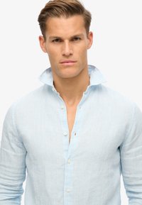 Lichtblauw gestreept overhemd met knopen, gemaakt van textuurstof, met een halfopen kraag en een iets ontspannen pasvorm. Klassieke knoopdetails inbegrepen.