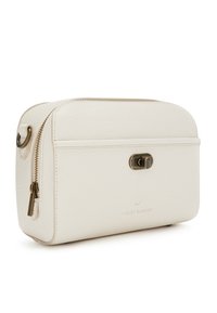 Cremfarbener Kosmetikkoffer mit glatter Textur, rechteckiger Form, oberem Reißverschluss und einer Messingbeschlägen. Mit geprägt Logo der Marke.