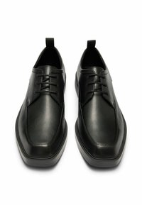 Scarpe in pelle nera con finitura texturizzata, punta arrotondata e tacco sollevato. Presentano un design con lacci e una linguetta ad anello alla punta.