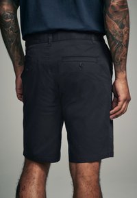 Dunkelmarineblaue Shorts aus leichtem Stoff, mit zwei Gesäßtaschen mit Knopfverschluss und geradem Schnitt, der oberhalb des Knies endet.