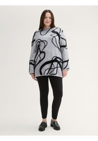 Un pull surdimensionné gris avec un design abstrait noir, doté de manches longues et d'un col rond, associé à des leggings côtelés noirs et des mocassins.
