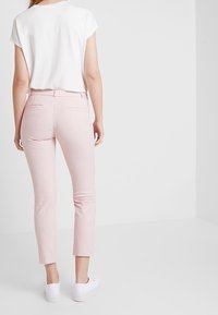 Light pink fitted trousers with a ribbed texture and cropped length, paired with a white short-sleeve top and white sneakers.