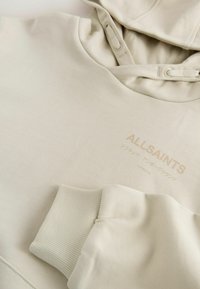 Béžová mikina AllSaints s príťahovými šnúrkami, rebrovými manžetami a logom, vrátane japonských znakov a "London" na hrudi.