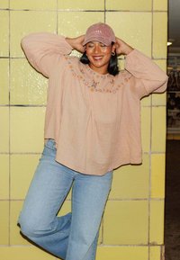 Blouse rose clair brodée avec des manches ballon, associée à un jean bleu. La personne porte une casquette en velours côtelé avec le texte "LOVER".