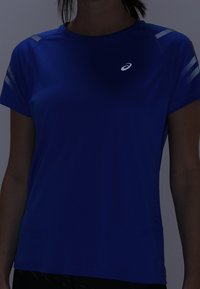 Modré atletické tričko z umělého materiálu s krátkými rukávy, reflexními prvky na ramenou a logem na hrudi.