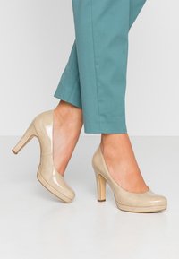 Décolleté beige in vernice con punta tonda e plateau, caratterizzati da una superficie liscia e un tacco a stiletto sottile.