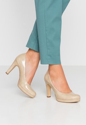 Beige patenterede højhælede sko med rund tå og plateau, der har en glat overflade og en slank stiletto hæl.