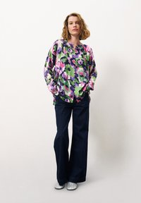 Florales Hemd mit Knöpfen in Grün, Lila und Pink, kombiniert mit dunklen Jeans und silbernen Glitzer-Stiefeletten. Lässiger Schnitt, lange Ärmel und runder Saum.
