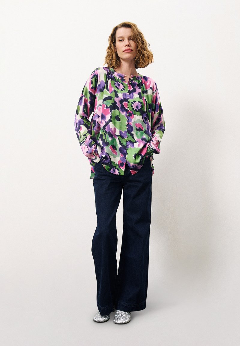 Florales Hemd mit Knöpfen in Grün, Lila und Pink, kombiniert mit dunklen Jeans und silbernen Glitzer-Stiefeletten. Lässiger Schnitt, lange Ärmel und runder Saum.