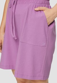 Lavendelfarbene Shorts aus strukturiertem Stoff mit einem elastischen Bund, seitlichen Taschen und einem kleinen Logo in der unteren Ecke.
