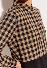 Koszula zapinana na guziki w kolorze beżowym i czarnym, z kołnierzykiem i długimi rękawami. Lekka tkanina o luźnym kroju i skróconym dole.