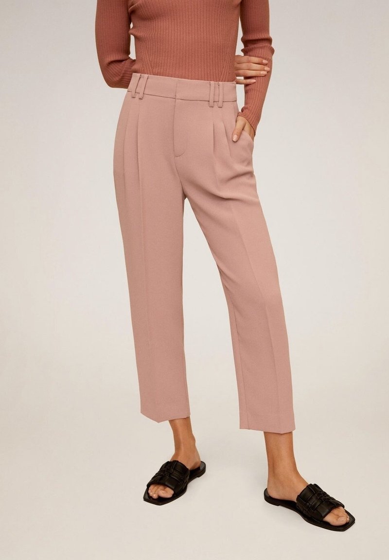 Pantalones de algodón rosa claro, con un corte recto, pliegues y trabillas para cinturón. Combinados con sandalias negras de pala; arriba, una blusa de manga larga de canalé.