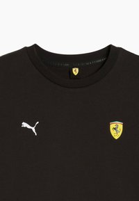 Sort crewneck t-shirt med hvid Puma-logo på venstre bryst og gult Ferrari-skjoldlogo på højre bryst.