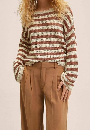 Femme portant un pull en tricot à rayures horizontales beige et marron, rentré dans un pantalon taille haute camel plissé avec des poches.
