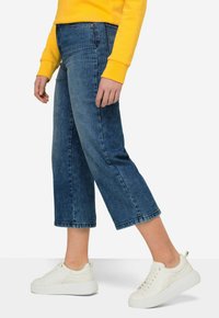 Jeans de denim azul claro cortados, con corte recto, que presentan un ribete vertical y un dobladillo sin terminar, combinados con zapatillas blancas.