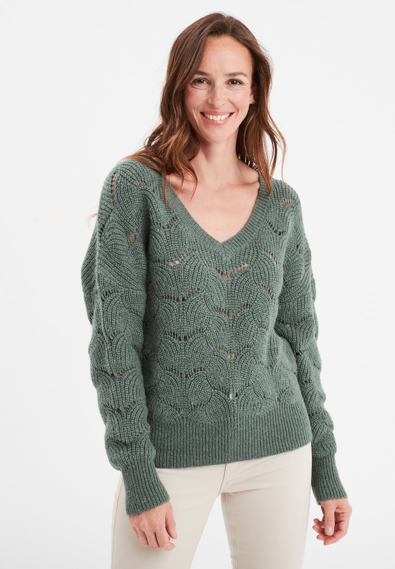 Pull en tricot vert à col en V, avec un motif en écailles texturé et des poignets côtelés. Détails en fil épais et doux qui améliorent le design.