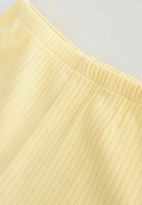 Tela acanalada amarilla con una cintura elástica, que presenta finas líneas verticales para textura. Acabado suave y material blando.