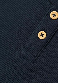 Tumes ribade kangast polo, kus on kaks beeži nuppu krae juures, mis omab tekstureeritud pinda ja detailset õmblust ääres.