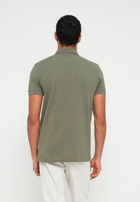 Oliwkowa zielona koszulka polo z krótkimi rękawami, prążkowanym kołnierzykiem i gładkim wzorem. Tkanina wydaje się gładka i lekka. Brak widocznych wzorów lub logo.