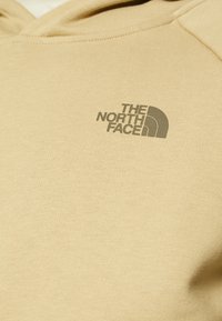 Felpa con cappuccio beige realizzata in morbido tessuto misto cotone, con un logo grigio di "The North Face" sul fronte. Tessuto liscio e vestibilità comoda.