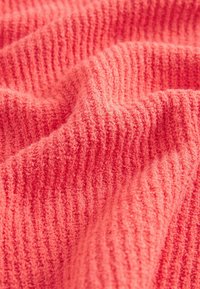 Tissu tricoté rose corail doux montrant une texture côtelée et des plis doux en gros plan.