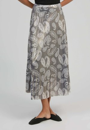 Femme portant une jupe grise taille haute, longueur cheville, avec des motifs cachemire blancs et des chaussures noires pointues sans lacets.