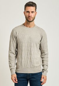 Maglione a maglia grigio chiaro con un motivo geometrico testurizzato, scollo rotondo e polsini e orlo a costine, abbinato a jeans blu scuro.