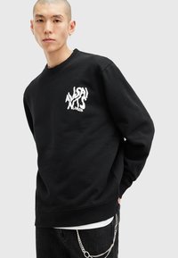 Sort fleece sweatshirt med rund hals, der har et hvidt grafisk logo på brystet. Blød tekstur og afslappet pasform.