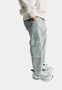 Lichtgroene flodderige cargobroek met zijzakken, gecombineerd met witte en mintgroene sportschoenen met mesh- en rubberdetails.