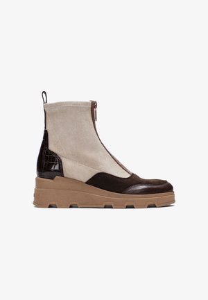 Bottine à talon compensé en suède beige et marron, dotée d'une finition en cuir patiné marron, d'une fermeture éclair sur le côté et d'une semelle en caoutchouc texturée marron.