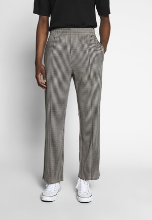 Pantalons à motif pied de poule noir et blanc avec une coupe décontractée, dotés de poches latérales et d'un design de jambe droite. Portés avec des baskets blanches.