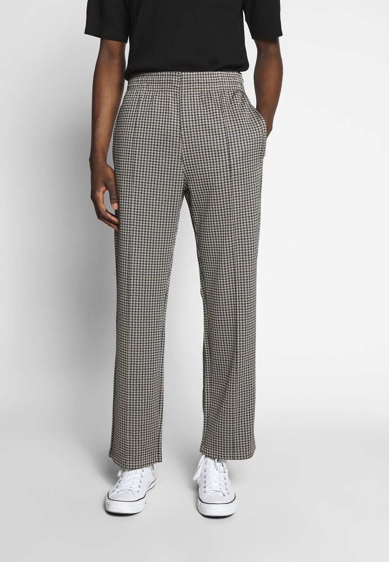 Černobílé kalhoty s kostkovaným vzorem houndstooth v uvolněném střihu, s bočními kapsami a rovnými nohavicemi. Nosené s bílými teniskami.