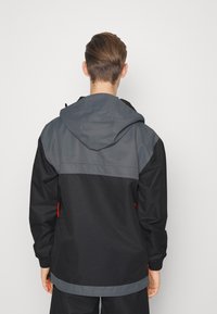 Mustat ja harmaat hupparitakkia, jossa on kaksivärinen muotoilu. Takissa on säädettävät narut, joustavat hihansuut ja sileä tekstuuri.