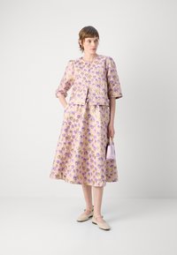 Abito a fiori di colore lilla con maniche corte e gonna svasata. Abbinato a scarpe beige e a una piccola borsa lavanda.