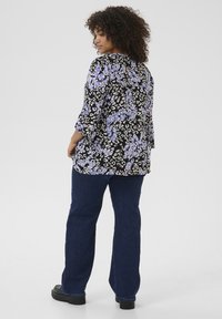 Sort top med lilla og hvide blomster mønster, trekvartærmer, parret med mørkeblå jeans og sorte platåsko.