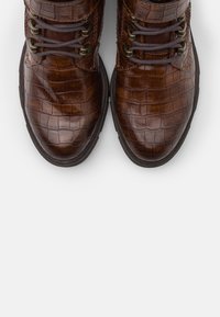 Bottes bottines en cuir marron avec un motif peau de crocodile, bout arrondi et lacets contrastants maintenus par des œillets en métal. Semelle plate en caoutchouc.