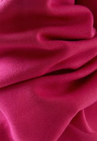 Tela elástica fucsia con una textura suave, que muestra pliegues drapeados y un brillo sutil. Ideal para aplicaciones de ropa o tapicería.