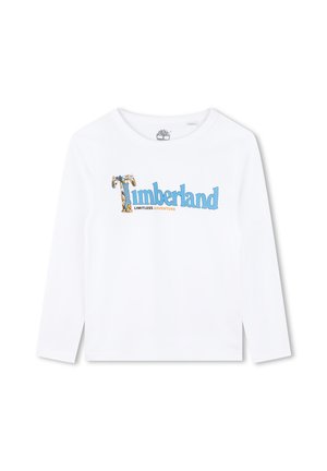 Camiseta de manga larga blanca con el texto "Timberland" en azul y naranja, con un gráfico de un árbol que acentúa el diseño. Material de algodón suave.