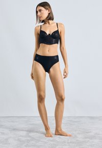 Set de lenjerie neagră, format dintr-un bralette din dantelă transparentă cu sârma de susținere și chiloți cu talie înaltă asortați, ambele împodobite cu modele intricate.