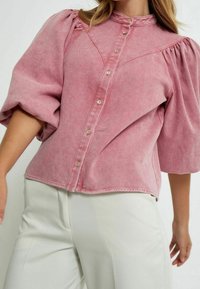 Rosé-färgad denimskjorta med puffärmar, knappstängning framtill och strukturerad yta. Framträdande vertikala sömmar och hög krage.