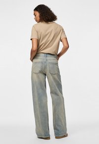 T-shirt marron clair à manches courtes associé à un jean en denim bleu délavé à jambes larges. Le jean présente des poches arrière classiques et une coupe décontractée.